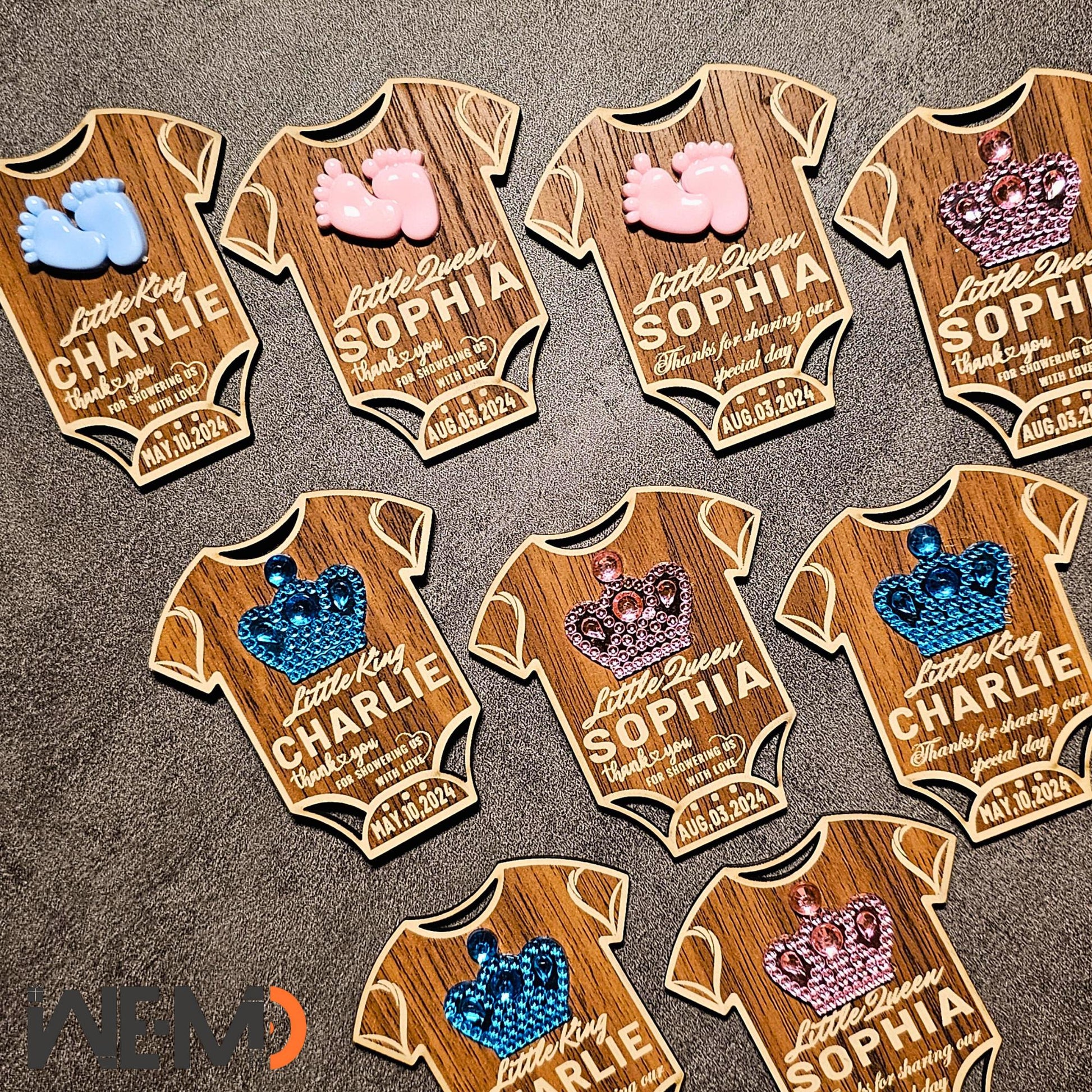 Top-down view of multiple baby magnets arranged by design. Each is engraved with name and date, with optional messages. These custom baby favors are great for guests, fridge magnets, or table decorations for baby parties.
