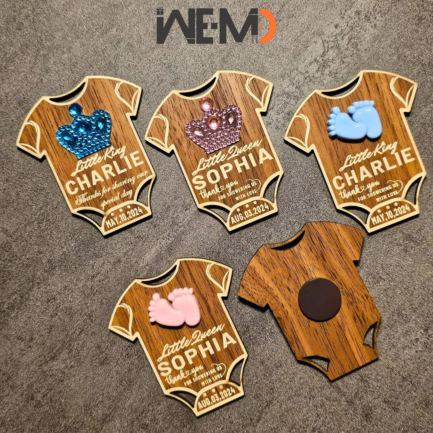 Top-down view of multiple baby magnets arranged by design. Each is engraved with name and date, with optional messages. These custom baby favors are great for guests, fridge magnets, or table decorations for baby parties.

