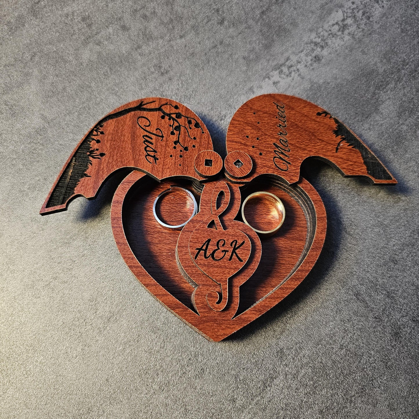 A close-up of a custom engraved wedding ring box in heart shape with both lids open, revealing two inner ring slots and personalized initials (A&K). This wooden ring holder is perfect for weddings, proposals, engagement shoots, or anniversary celebrations. A romantic gift box, laser cut from natural wood, ideal as a unique keepsake box for couples. Popular as a rustic wedding ring box, engraved engagement gift, or couple’s anniversary present.