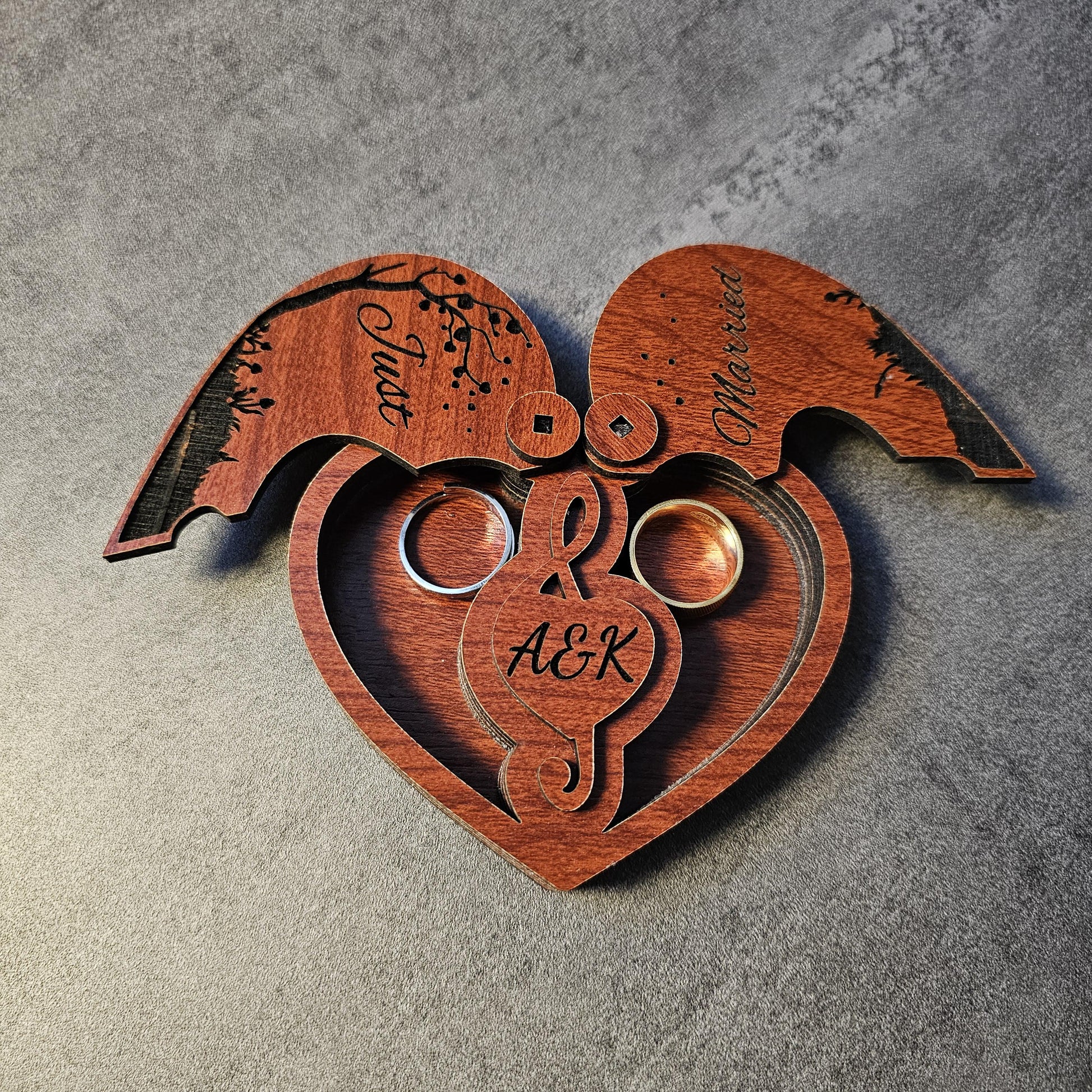 A close-up of a custom engraved wedding ring box in heart shape with both lids open, revealing two inner ring slots and personalized initials (A&K). This wooden ring holder is perfect for weddings, proposals, engagement shoots, or anniversary celebrations. A romantic gift box, laser cut from natural wood, ideal as a unique keepsake box for couples. Popular as a rustic wedding ring box, engraved engagement gift, or couple’s anniversary present.